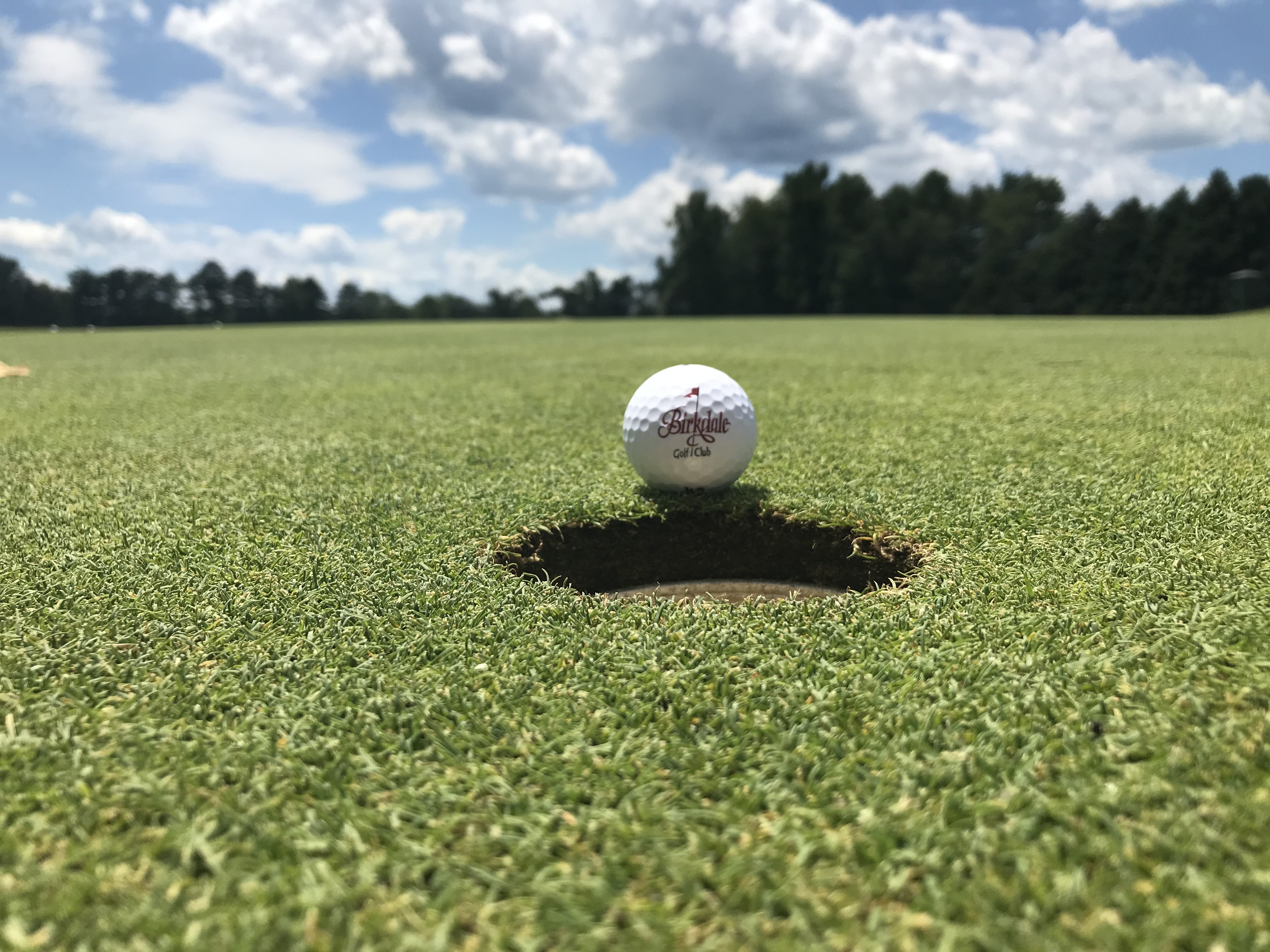 A Birkdale golf ball beside the cup on a putting green