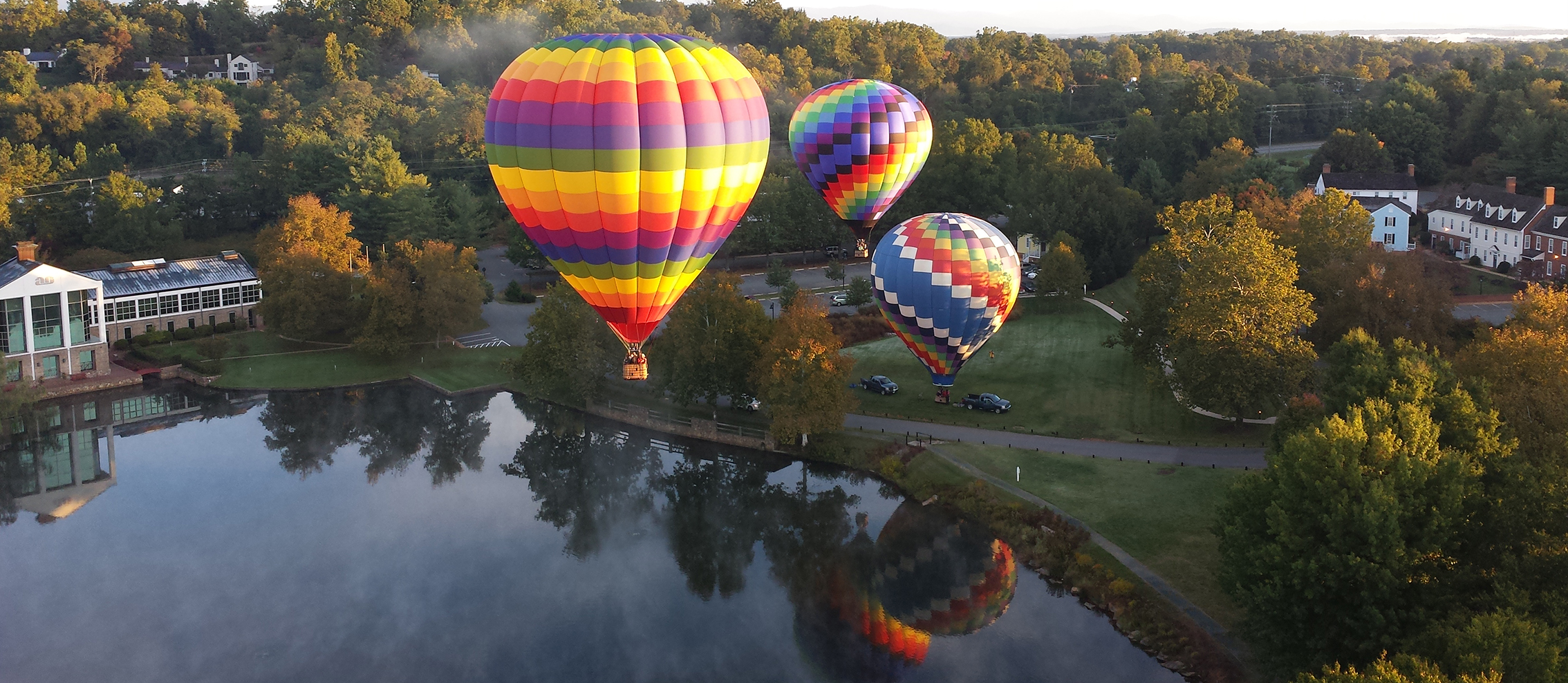 Three colorful hot air balloons floating over a lake and autumn trees